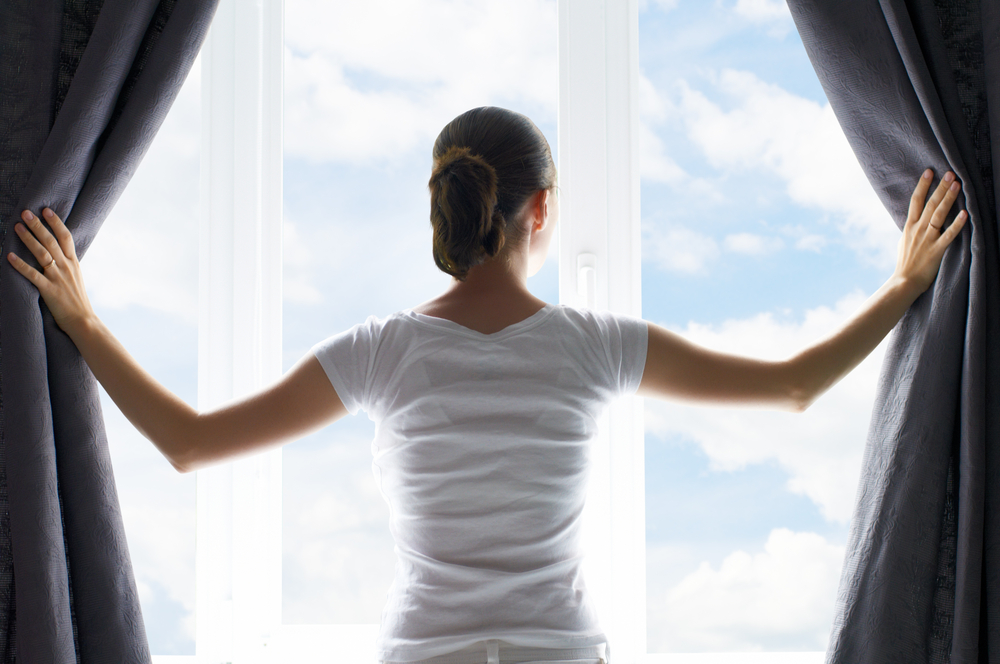 Woman opens curtains to let sunlight into heat home